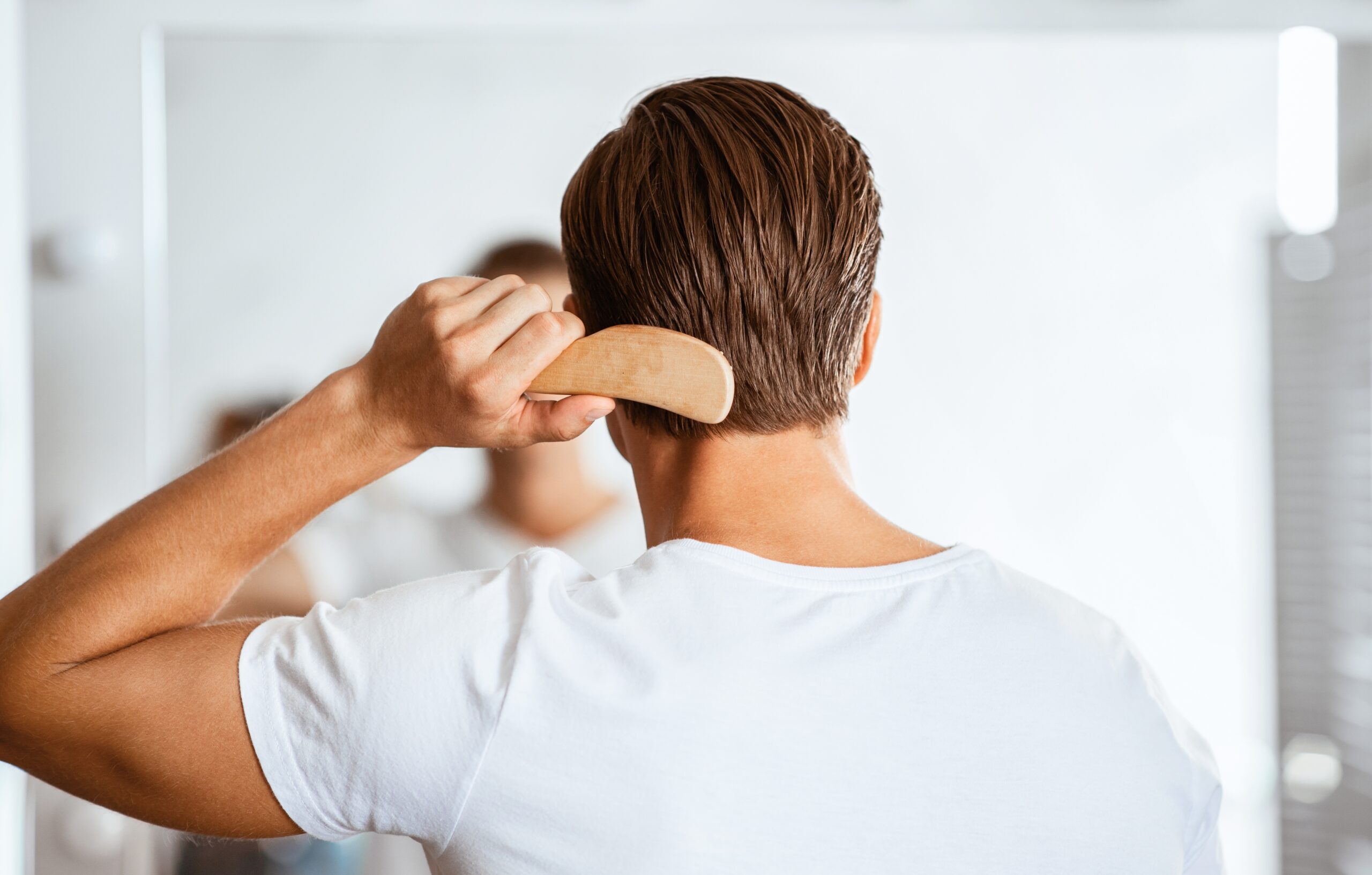 Man checking the back of his hair in a mirror with a comb.