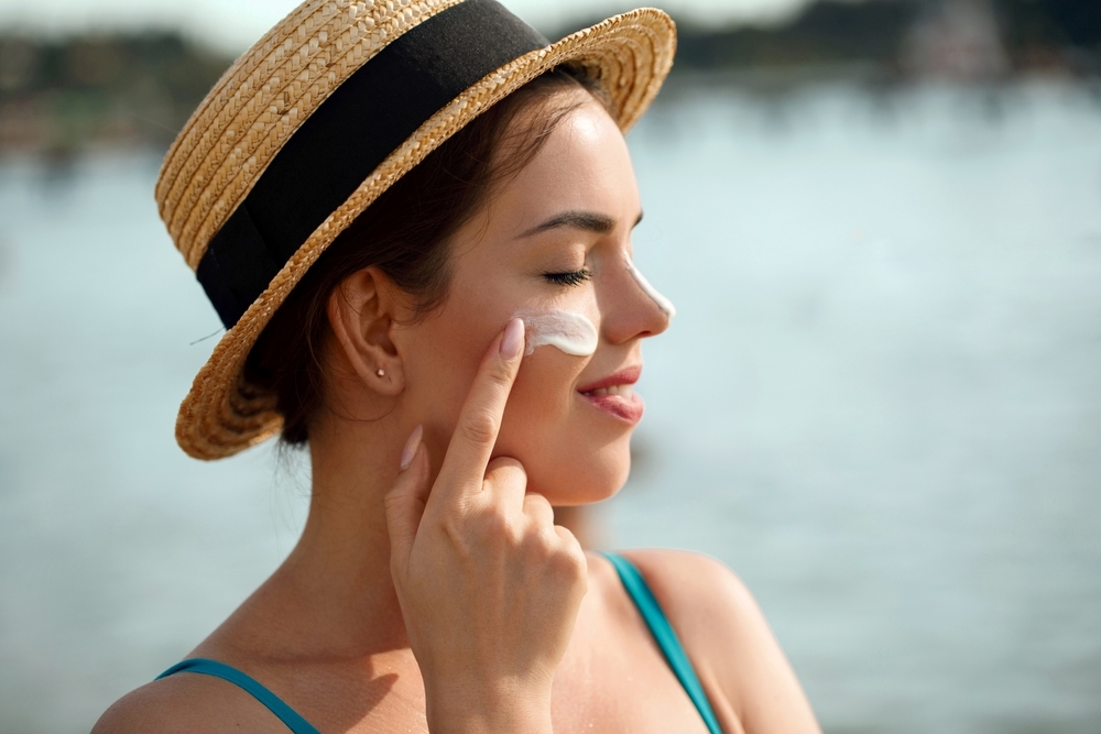 A woman applying sunscreen to her face for post-treatment skin care.