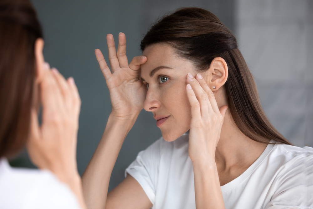 Close-up of a woman examining her eye area in a mirror