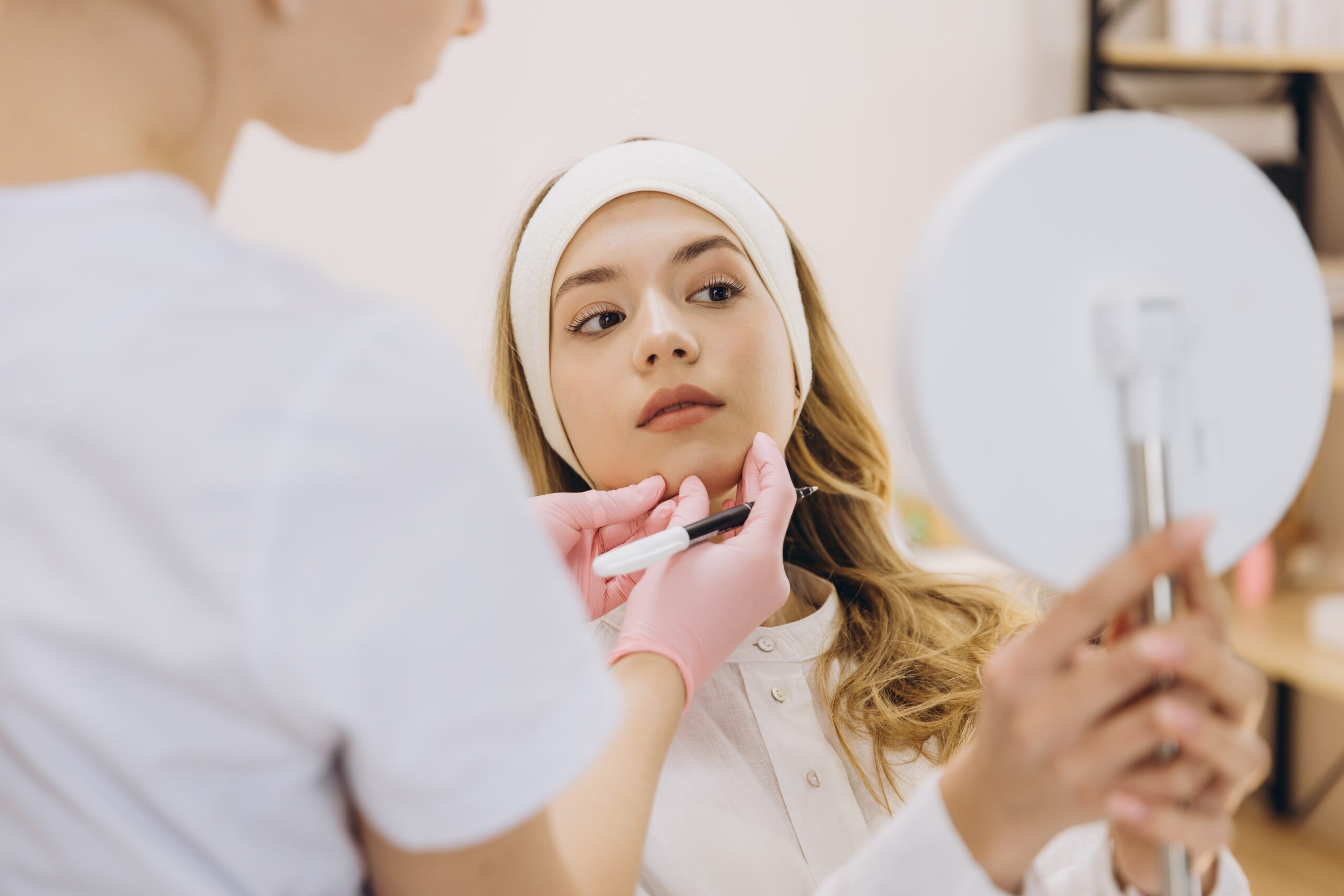 A doctor conducting a facial consultation with a patient holding a mirror to discuss treatment options.