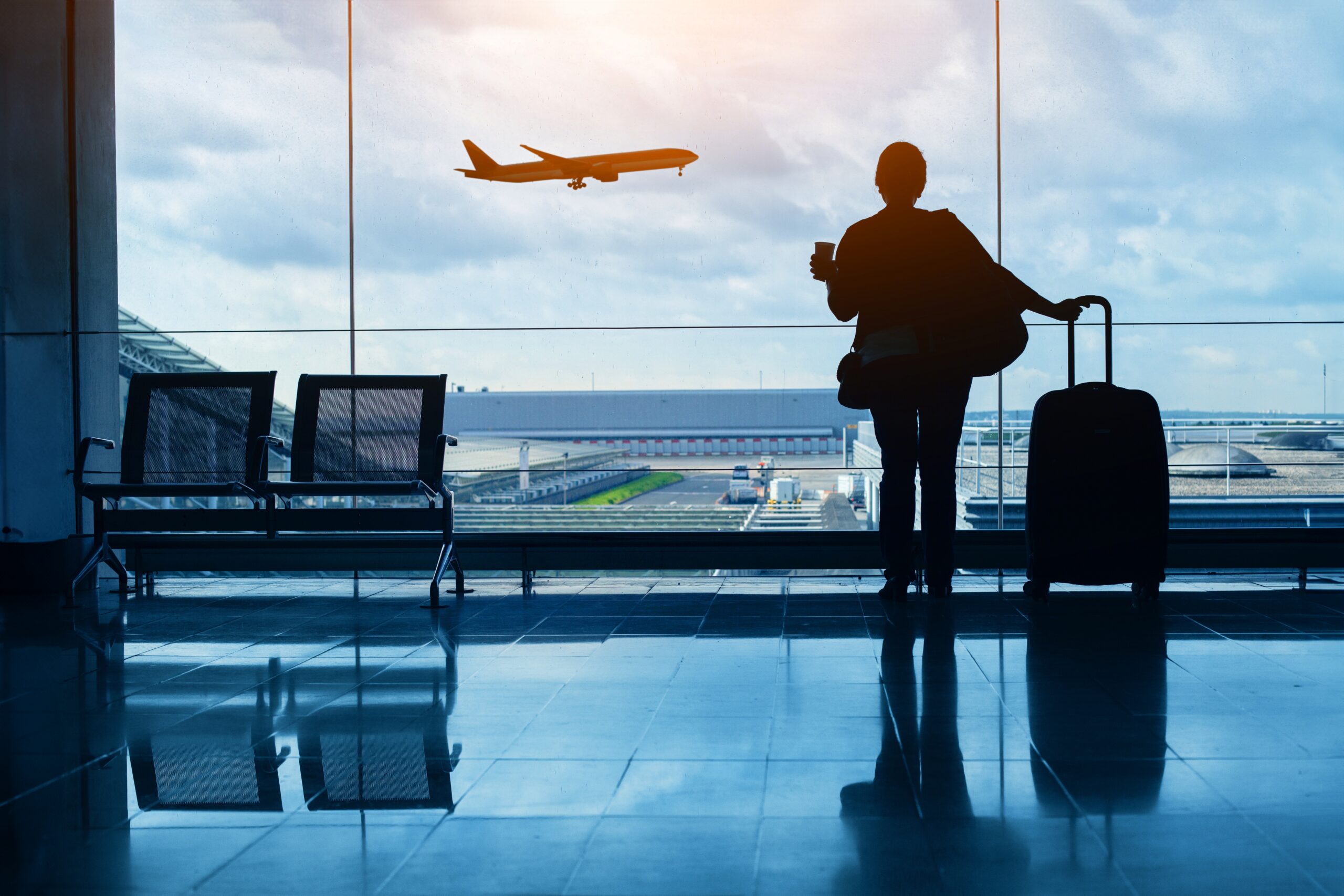 Person looking at an airplane through an airport window with luggage