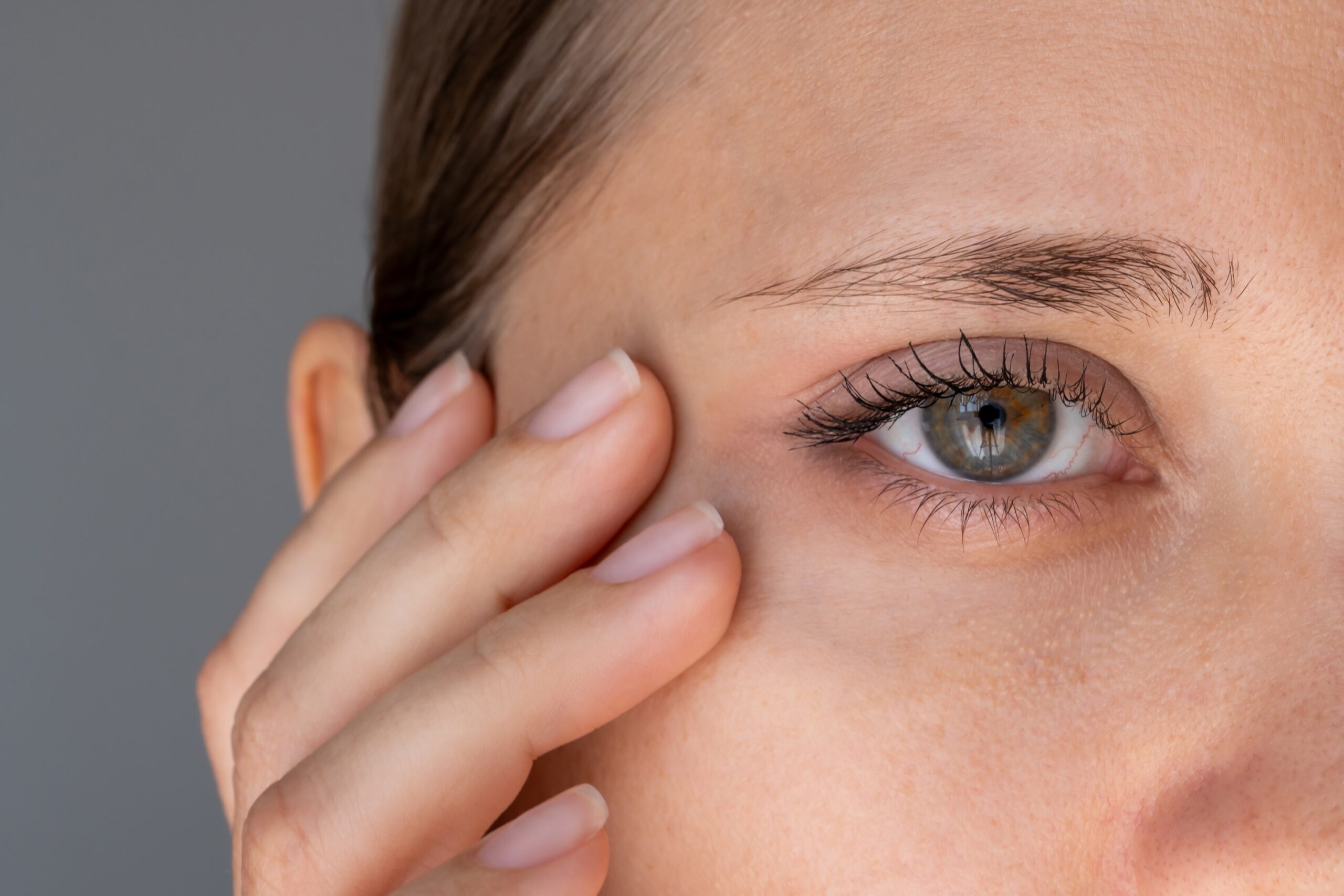 Close-up of a woman checking the skin texture and contour beneath her eye.