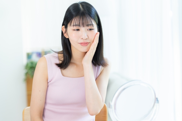 鏡を見ながら頬に手を当てる女性　テオシアルとジュビダームの違いは？仕上がり・持続・安全性を比較｜NERO DOCTOR / BEAUTY（美容医療）