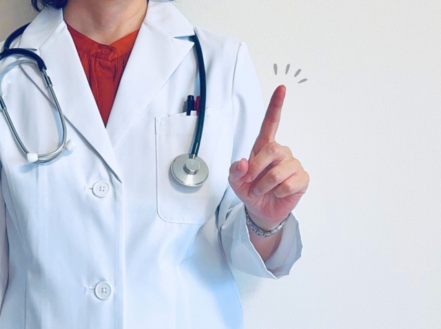 人差し指を立てる白衣の女性　前額リフトで額・眉間・まぶたをまとめて若々しく？切開式と内視鏡的リフトの違い｜NERO DOCTOR / BEAUTY（美容医療）