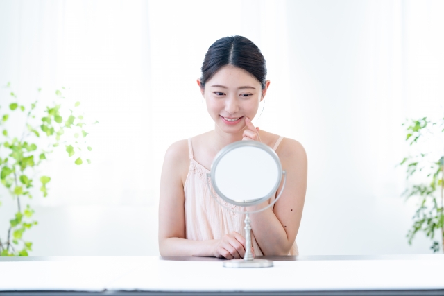 鏡を見て微笑む女性 口角挙上で芸能人みたいな口元になれる?写真の「真実」と施術の現実|NERO DOCTOR / BEAUTY(美容医療)
