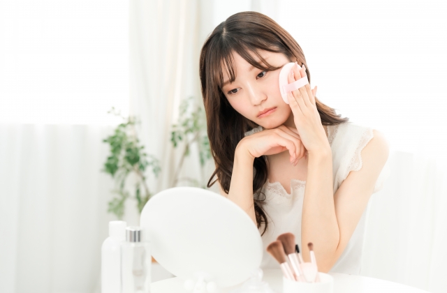 浮かない顔でメイクする女性 頬骨が出てるのが気になる人へ|原因と美容医療の選択肢|NERO DOCTOR / BEAUTY(美容医療)