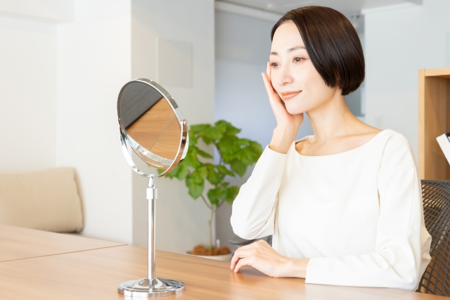 鏡を見ながら頬に手を当てる女性　リバースエイジングはどこまで本当？生物学的年齢、老化時計、できること・できないこと｜NERO DOCTOR / BEAUTY（美容医療）