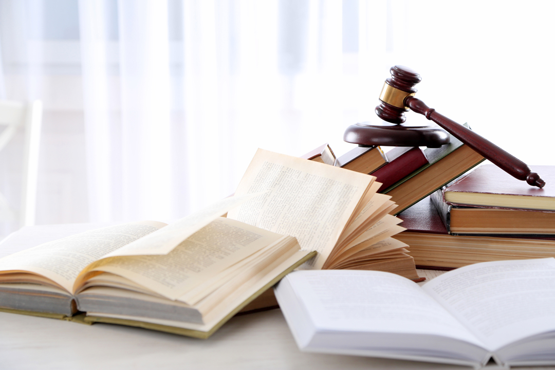 開かれた古い本の上に置かれた、法律や裁判を象徴する木製のガベル(小槌)