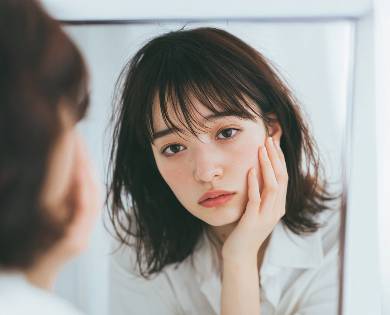 鏡を見ながら悩む女性のイメージ画像