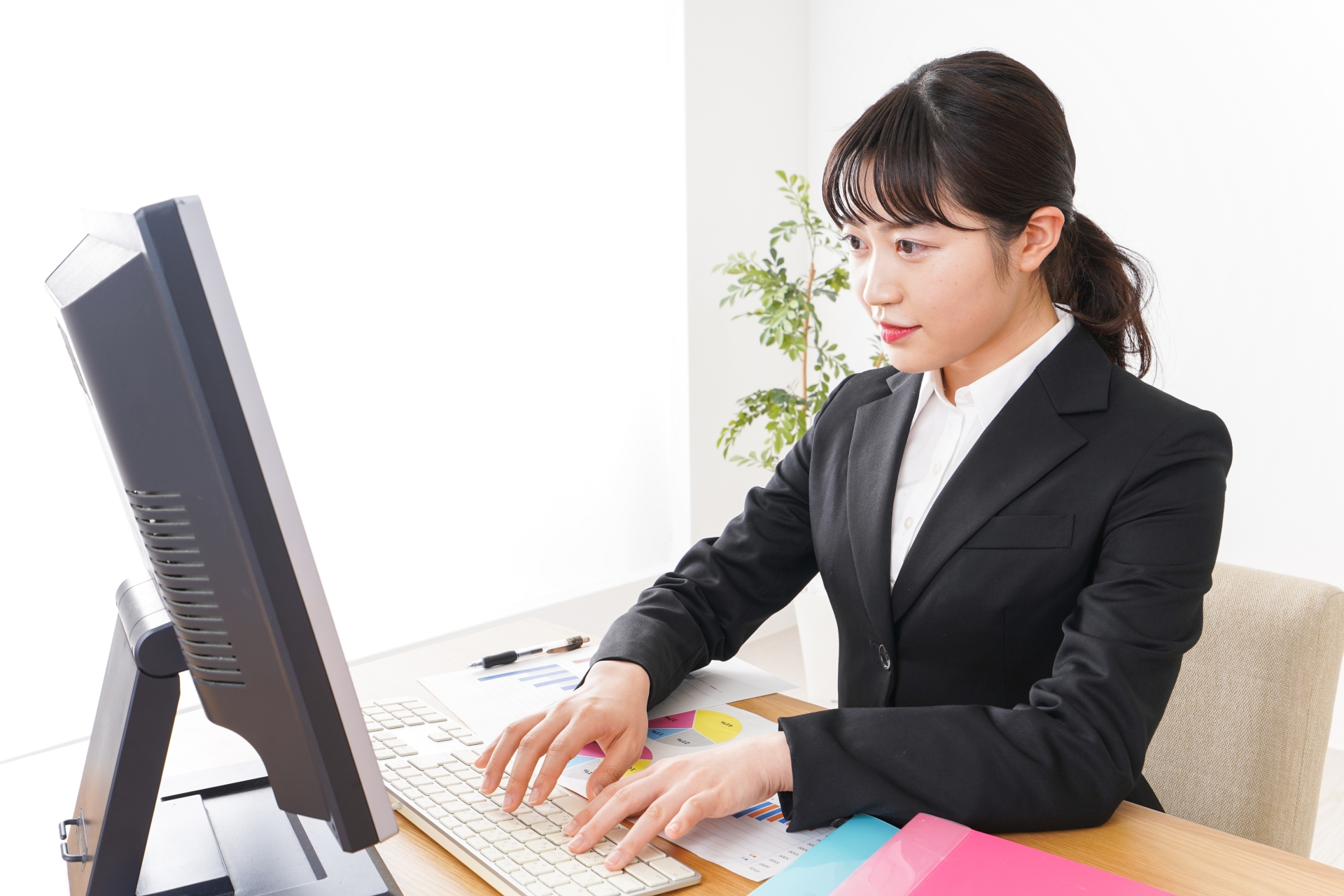 オフィスのデスクでパソコンの画面を見つめながらキーボードを叩くスーツ姿の女性