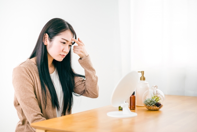 眉間のシワに鏡を見ながら悩んでいる女性の画像