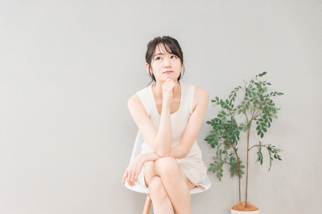 太ももの脂肪吸引の料金やクリニック選びについて、椅子に座ってあごに手を当てて悩む女性