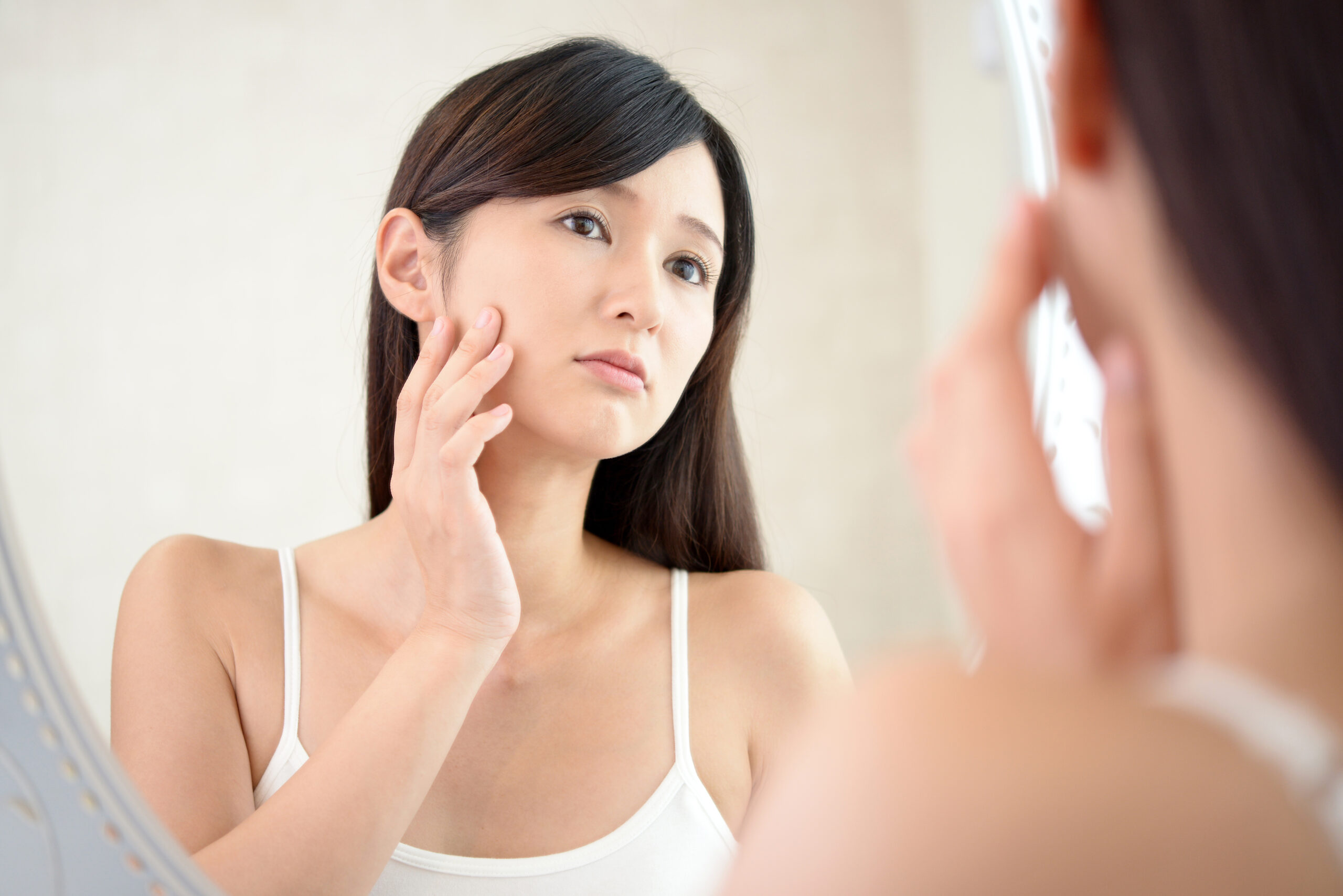 鏡を見ながらたるみやほうれい線に悩む女性