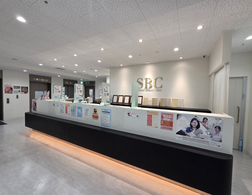 湘南美容皮フ科 新宿東口院の受付。リブランディング前の院内環境。 白を基調としたカウンターに案内表示やポスターが並ぶ